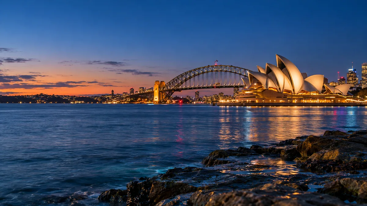 Sydney Harbour landmarks at dusk, with warm light reflected on blue water.